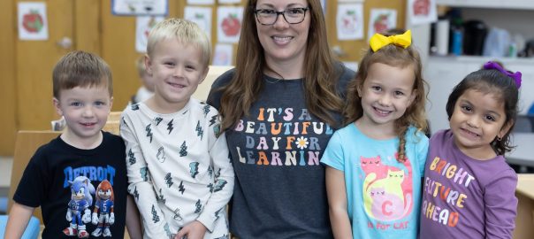 Four young children surround a smiling teacher at St. Charles Borromeo Catholic School in Greenville, Michigan.